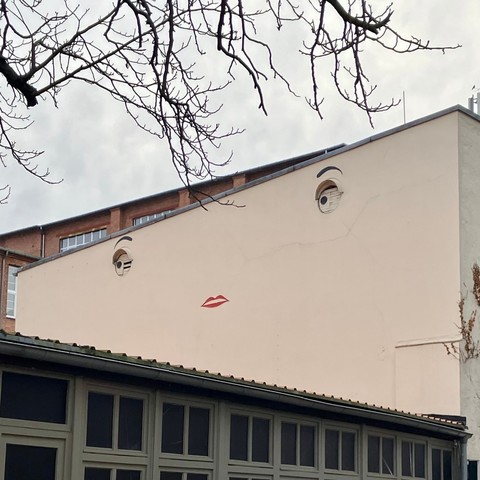 Zwei Fensterluken sind wie Augen gestaltet, darunter ist ein Kussmund gemalt