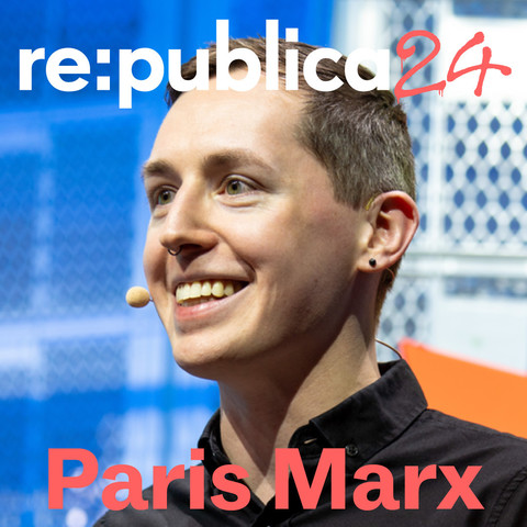 Canadian author, podcast host and journalist Paris Marx stands on a re:publica stage, wearing a headset and looking past the camera into the audience. 