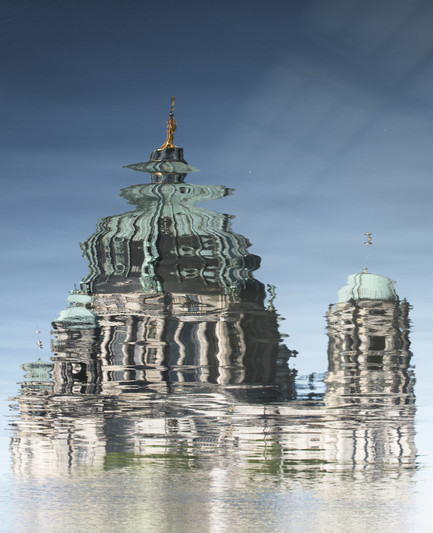 Reflection of a church in the water, creating wave like patterns of the architecture with blue sky  in the background. 