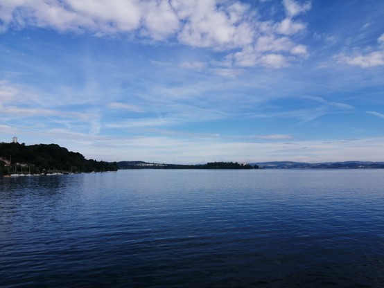 Blue sky with few clouds over the lake.

On the left, a hill with trees and a church on top. 
