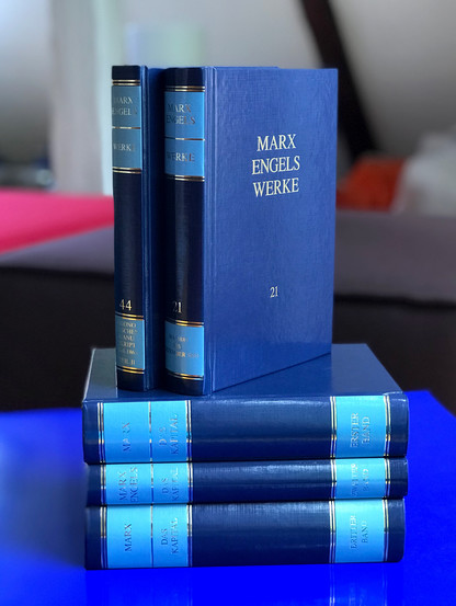 Aufeinandergestapelte blaue Bände unserer Marx-Engels-Werke (MEW), die neben anderen im Interview vorkommen: Das Kapital Erster Band / Zweiter Band / Dritter Band, MEW Band 44 / MEW Band 21