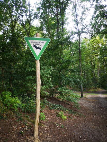 Ein Schild, auf dem Landschaftsschutzgebiet steht. Rechts daneben beginnt ein Weg in den Wald. 