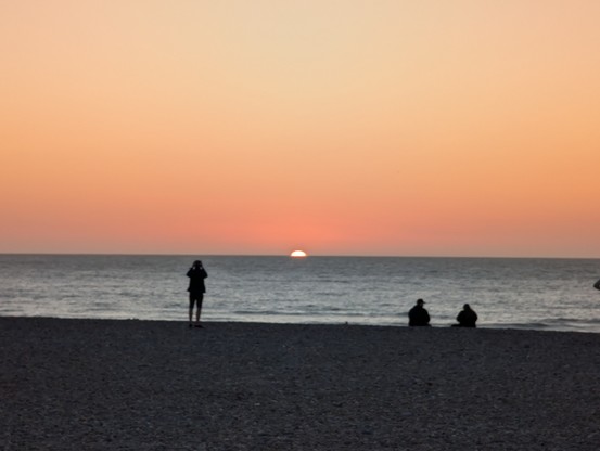 Personen stehen an der Küste und beobachten den Sonnenuntergang am Meer