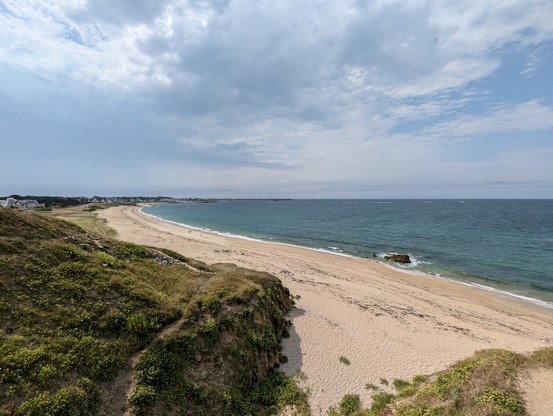 Ein langgezogener leerer Sandstrand mit türkisblauem Wasser und Dünen