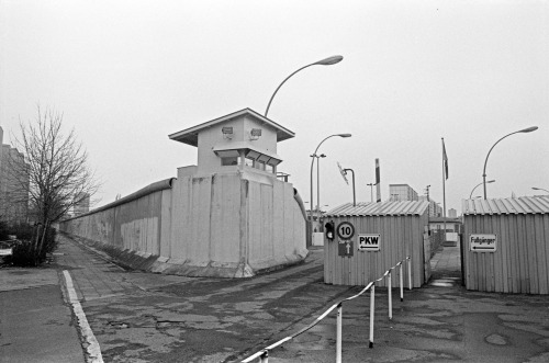 Ein Schwarz-Weiß-Foto mit Berliner Mauer, Wachturm und dem ehemaligen Grenzübergang Heinrich-Heine-Straße.